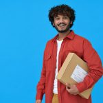 Happy indian young man holding parcel box isolated on blue background.