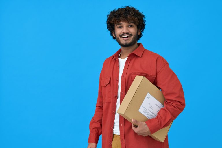 Happy indian young man holding parcel box isolated on blue background.