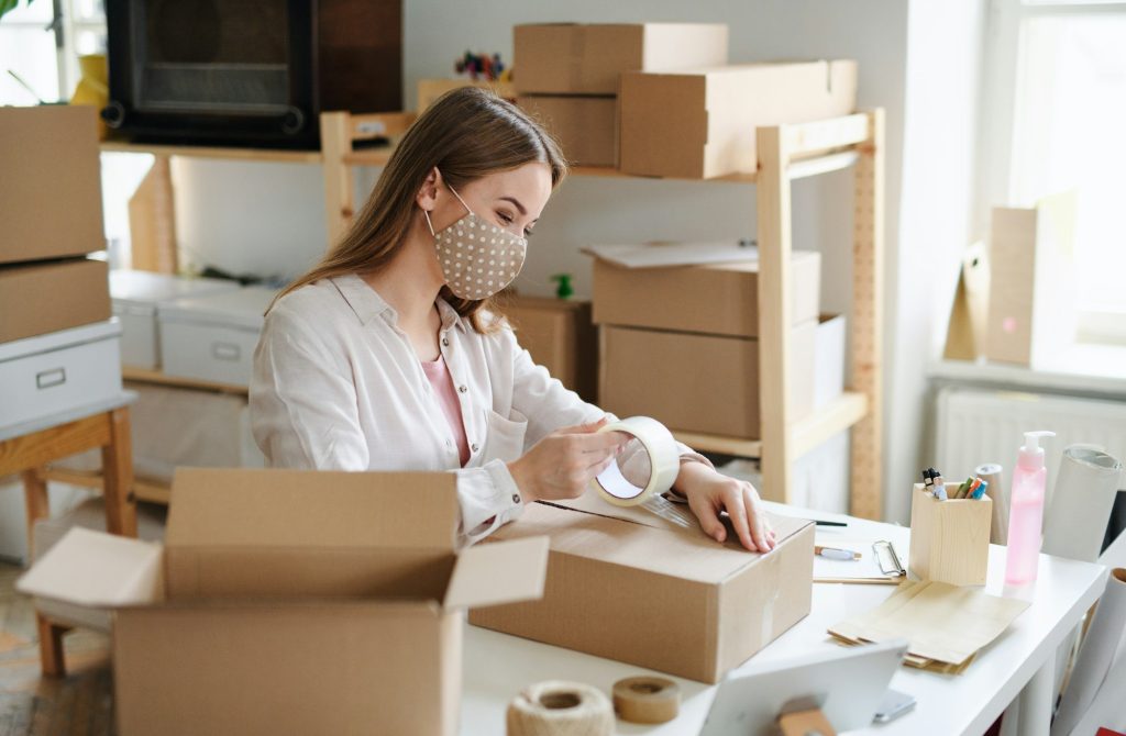 Woman dropshipper working at home, packing parcels. Coronavirus concept.