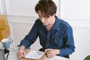 Asian male business owner packing package preparing delivery parcel and attaching data label