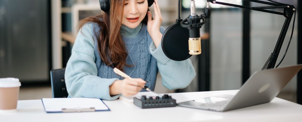 Asian woman wearing headphones and doing a live podcast for their channel, communication
