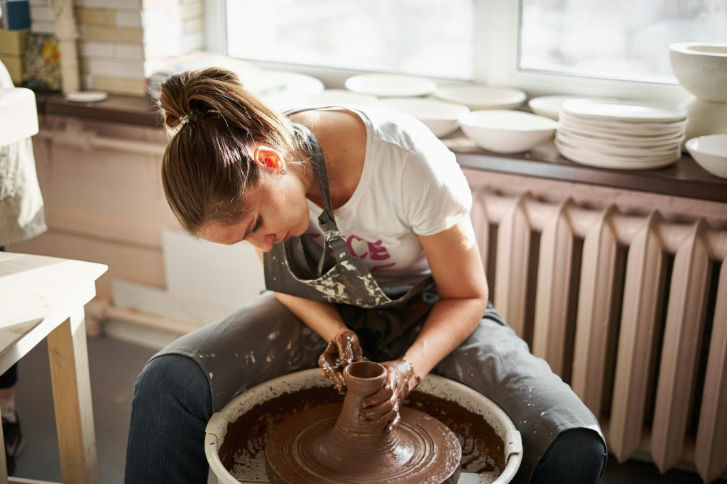 Beautiful woman making ceramic pottery on wheel, hands close-up. Concept for woman in freelance