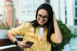 Female blogger in stylish wear using a smartphone in a public place. Technologies and people concept