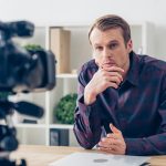 handsome pensive male video blogger recording vlog in office