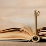 Retro key and opened book on wooden table.