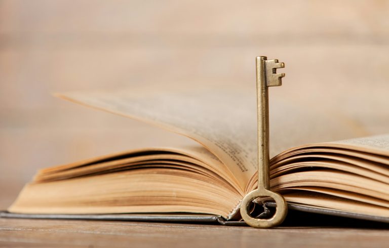Retro key and opened book on wooden table.