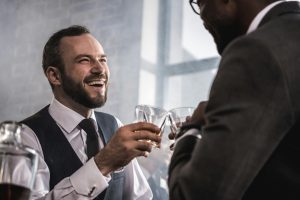 Two businessmen in formal wear clinking whiskey glasses and talking