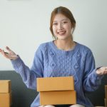 Woman happily holding shipping box, surrounded by packages. Concept of online shopping