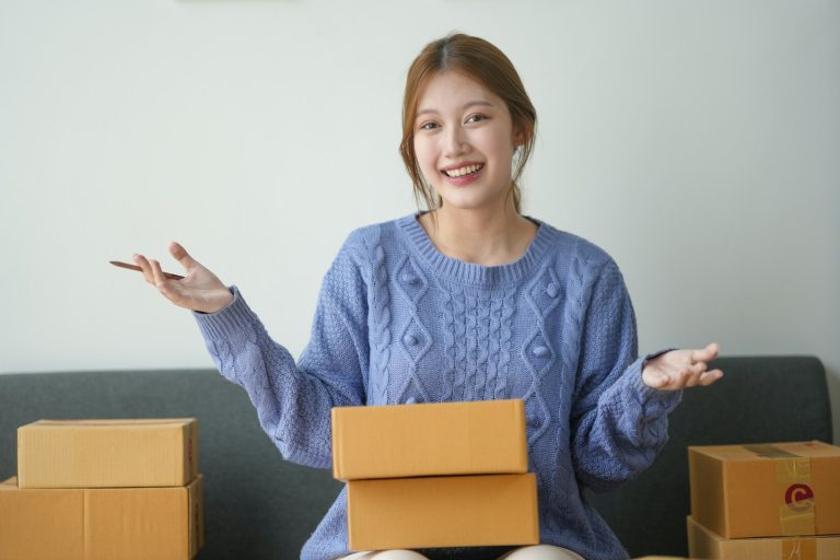 Woman happily holding shipping box, surrounded by packages. Concept of online shopping
