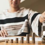 Woman's hand. Put a coin into a glass bottle with coins, saving money with coins, stepping into