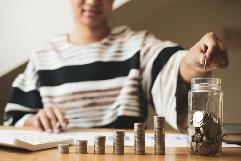 Woman's hand. Put a coin into a glass bottle with coins, saving money with coins, stepping into