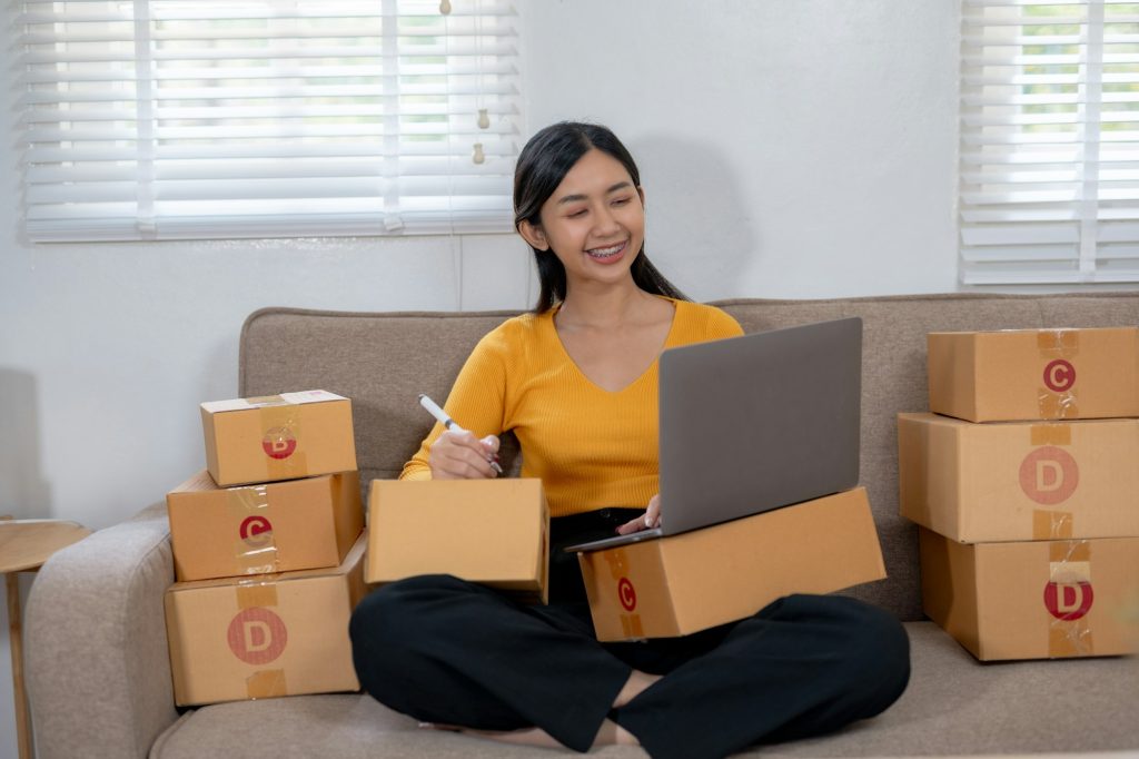 Woman working on a laptop and holding a pen, surrounded by packages.