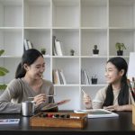 Asian mother painting picture with daughter in living room.