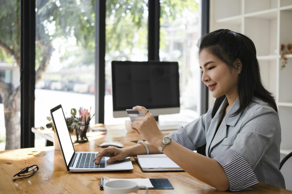 Beautiful young woman holding credit card and making payment online on laptop computer.