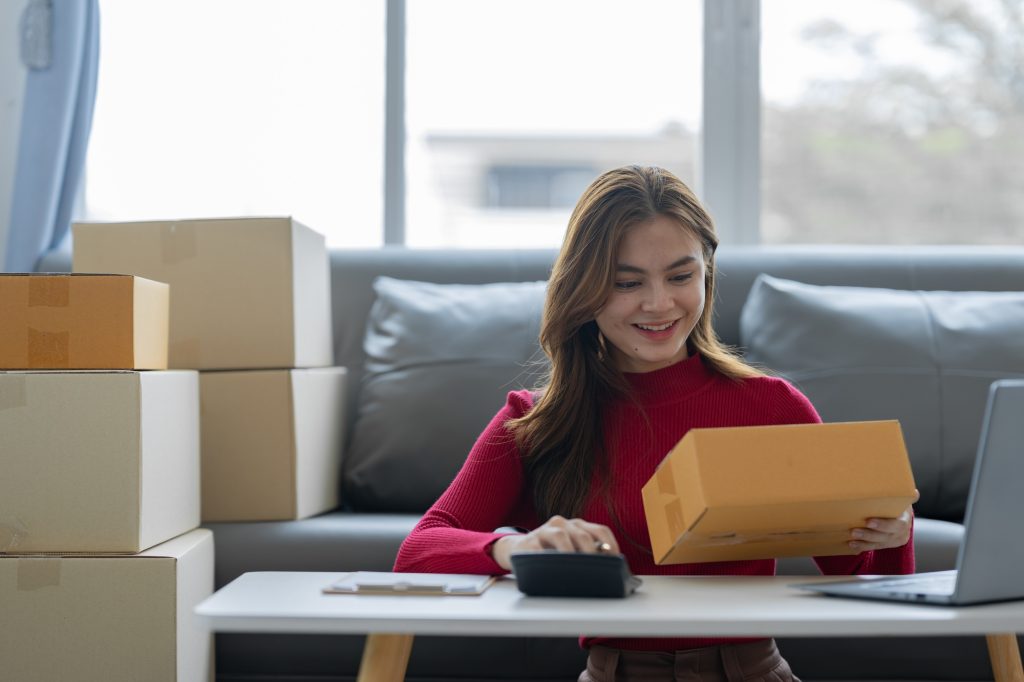 female online seller online shop use calculator and a laptop to calculate the cost before packaging