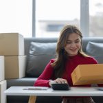 female online seller online shop use calculator and a laptop to calculate the cost before packaging