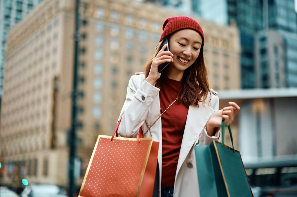 Happy Asian woman making phone call while shopping in the city,