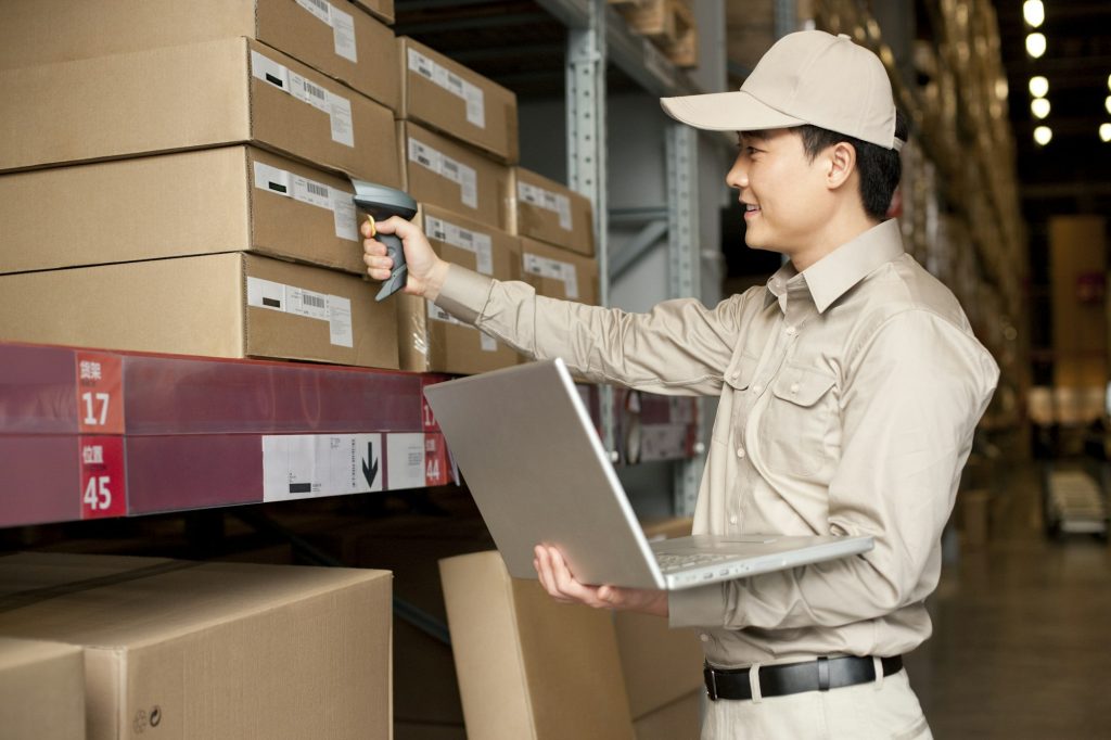 Male Chinese warehouse worker with laptop and scanner