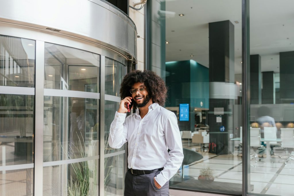 Smiling Businessman with Afro Hair Making a Phone Call Outside Modern Office Building