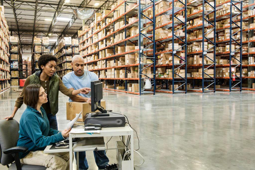 Warehouse workers checking inventory on a computer in a large distrubiton warehouse.