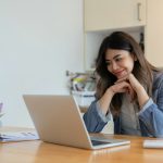 Young Freelance Woman Working from Home in Modern Kitchen, Smiling and Using Laptop, Remote Work