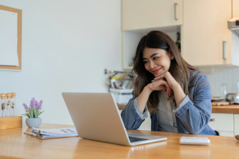 Young Freelance Woman Working from Home in Modern Kitchen, Smiling and Using Laptop, Remote Work