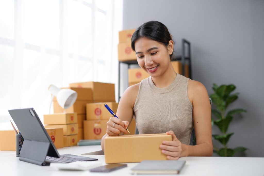 Young woman working on online business, packaging a box at a home office